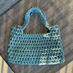 a crocheted blue purse sitting on top of a bed next to a pillow