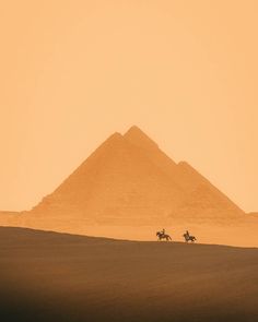 two people riding horses in front of the pyramids