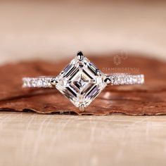 a diamond ring sitting on top of a piece of wood with leaves in the background