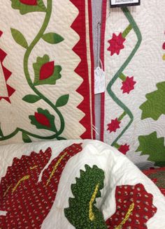 some very pretty quilts on display with red and green flowers in them for sale