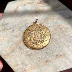 Lovely antique Art Nouveau locket, made in the early 1900s. It is made of yellow gold filled metal with a matte finish. The front features beautiful hand engraved flowers and leaves, while the back of the locket is plain. Inside of the locket are stamps "B. MFG. CO.", which I believe stands for Ballou Manufacturing Co, a jewelry company founded in Attleboro MA in the early 1900s. For its age, this locket is in very good condition. It does have some signs of wear, expected since it's over 100 years old and was likely well loved. The outside has faint surface scratches, age related patina, and 3 dents on the back (see photos 2 and 5 for reference) . On the inside of the locket, there is also patina and scratches. Both of the metal photo frames are present. The bail is secure and the locket c Victorian Flower Jewelry For Collectors, Victorian Flower Jewelry Collectible, Victorian Flower-shaped Collectible Jewelry, Victorian Flower Collectible Jewelry, Vintage Gold Jewelry With Etched Details, Antique Gold Flower Jewelry, Vintage Gold Etched Jewelry, Vintage Bronze 14k Gold Jewelry, Vintage 14k Gold Coin Jewelry