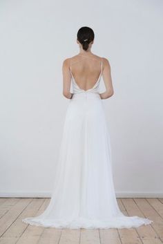 the back of a woman in a white wedding dress standing on a wooden floor with her back turned to the camera