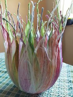 a close up of a vase on a table with many flowers in the center and leaves sticking out of it