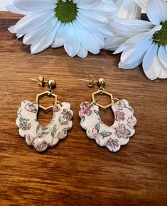 two white and pink flowered earrings on top of a wooden table next to flowers