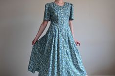 Vintage peasant floral summer dress with buttoned front and short sleeves, from the 1990s era Botanical summer dress with a fitted upper part and flare mid calf length. The dress has a floral pattern in blue and green and a buttoned front, made of lightweight cotton fabric. The dress has small shoulder pads and 2 hand pockets  Brand - Hammerschmid Size - marked 40 EU / 10 US, model in the photos wears 38 EU / 8 US, cup size A,  fits big! Please look at measurements as this is a vintage dress and Blue Prairie Dress For Summer, Vintage Summer Dress With Buttons For Garden Party, Summer Vintage Dress With Buttons For Garden Party, Cotton Floral Print Prairie Dress With Short Sleeves, Green Fitted Cottagecore Vintage Dress, Short Sleeve Floral Print Prairie Dress For Daywear, Floral Print Short Sleeve Prairie Dress For Daywear, Short Sleeve Prairie Dress With Floral Print For Daywear, Vintage Blue Prairie Dress For Summer