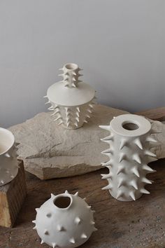 three white vases sitting next to each other on top of a wooden table with rocks