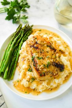 a white plate topped with chicken and mashed potatoes next to green asparagus