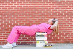 a woman in pink is leaning on a stack of books and looking up at the sky