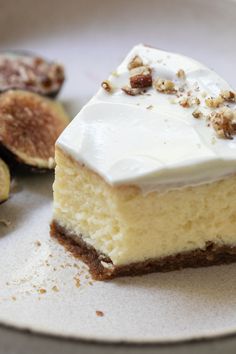 a piece of cheesecake with white frosting and figs on the side sitting on a plate