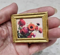 a hand holding a small gold frame with flowers on it