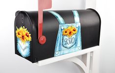 a mailbox with sunflowers painted on the front and side, sitting on a white wall