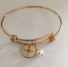 "This listing includes a gold plated stainless steel expandable bangle bracelet with a 1/2\" nu gold discs hand stamped with a compass paired with a Swarovski white pearl. Nu-gold is a copper alloy consisting of 85% copper and 15% zinc. It has a rich warm color and if highly polished resembles gold. This is also known as jewelers brass and will tarnish and need to be polished. What I would like you to know: All of my pieces are hand stamped and made with love just for you. They will arrive in a Compass Bracelet, Expandable Bangle Bracelet, A Compass, Gold Charm Bracelet, Copper And Brass, Gold Charm, Gold Gold, White Pearl, Bangle Bracelet