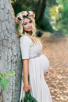 a pregnant woman leaning against a tree wearing a flower crown