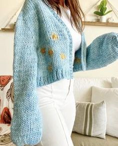 a woman in white pants and a blue sweater is holding her hand out to the side