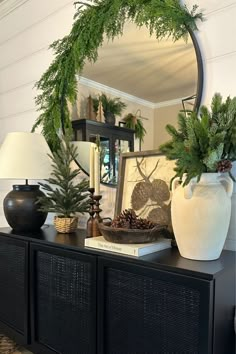 a mirror sitting on top of a dresser next to a vase filled with greenery