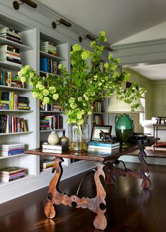 a vase with flowers on a table in front of a bookshelf filled with books