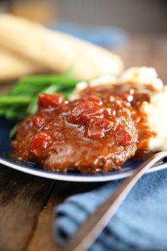 a close up of a plate of food with meat and sauce on it next to green beans