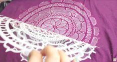 someone is cutting out some paper doily on a purple t - shirt with white lace