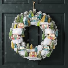 a christmas wreath hanging on the front door with snow around it and houses painted on it