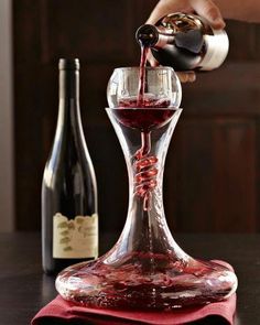 a person pouring red wine into a glass on top of a table next to two bottles