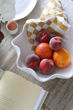 a bowl filled with fruit sitting on top of a table next to an open book