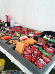 a table filled with lots of food on top of a grass covered field next to a white wall