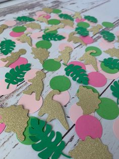 pink, green and gold paper cut outs with palm leaves on them sitting on a wooden surface