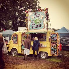 three people standing in front of a food truck at an outdoor event with tents and trees