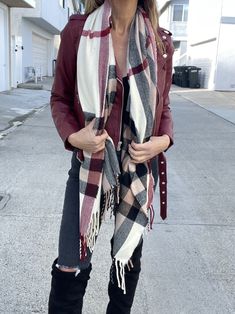 a woman wearing black boots and a red jacket is standing in the street with her scarf around her neck