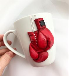 a hand holding a coffee mug with red boxing gloves on it