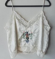 Free Hand embroidery upcycled on a vintage polyester lace camisole. Made in the USA; 100% polyester off white cropped camisole with lace trim. Size XL BUST 46" WAIST 46" SIDE LENGTH 12" Cropped Lace Tank Top, White Embroidered Cami Tank Top, Lace Crop Top Tank With Lace Trim, Lace Crop Top With Lace Trim, Vintage Lace Camisole For Spring, Cropped Lace Tank Top With Lace Trim, Lace Cami Crop Top With Lace Trim, White Floral Embroidery Camisole Tank Top, Vintage Tops With Lace Trim And Spaghetti Straps