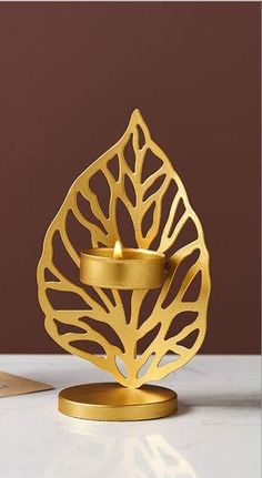 a gold candle holder with a leaf design on it and a card in the background