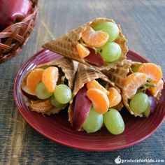 some fruit and crackers are on a red plate next to an empty basket full of oranges