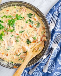 a skillet filled with cheese and vegetables on top of a blue towel next to silverware