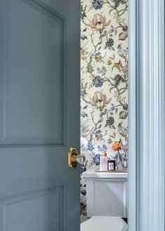 an open door leading to a bathroom with floral wallpaper on the walls and a white toilet