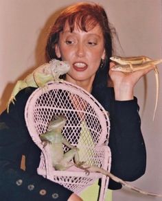 a woman holding two small birds in her hands and one bird on top of the chair