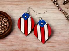 These handmade, hand-painted wooden earrings are a vibrant celebration of Puerto Rican pride. Crafted with meticulous attention to detail, each pair features the iconic Puerto Rican flag, delicately depicted across two hanging parts that move gracefully with the wearer. The design thoughtfully symbolizes a deep connection to Puerto Rican heritage, showcasing the flag's bold colors and meaningful symbols. These earrings hang from hypoallergenic, lead and nickel-free findings, ensuring they are safe and comfortable for even the most sensitive ears. Whether for a special occasion or everyday wear, these earrings are a perfect way to honor and express pride in being Puerto Rican. Patriotic Multicolor Earrings For Independence Day, Patriotic Multicolor Earrings As Gift, Multicolor Earrings For Independence Day Gift, Patriotic Handmade Earrings For Gift, Patriotic Handmade Earrings As A Gift, Independence Day Dangle Earrings As Gift, Independence Day Gift Dangle Earrings, Independence Day Dangle Earrings Gift, Puerto Rican Heritage