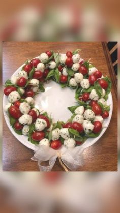 a wreath made out of tomatoes and mozzarella on a white plate with ribbon