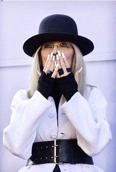 a woman with white nails and black hat covering her mouth