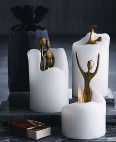 two white candles with gold figurines on them, one holding a woman's hand