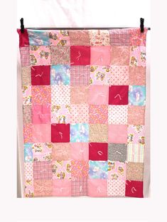 a pink and red patchwork quilt hanging on a wall in front of a white background