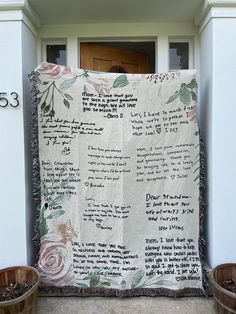 a large quilt hanging from the side of a building next to two buckets filled with flowers