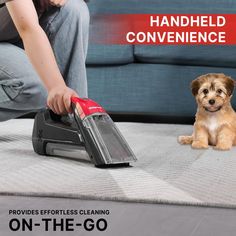 a woman kneeling down next to a dog on the floor with a vacuum in front of her