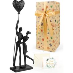 a figurine holding a heart shaped balloon next to a gift box and card