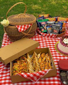 a picnic table with food and snacks on it, including cake in a box as well as other items