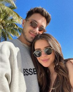 a man and woman standing next to each other in front of palm trees on the beach