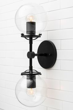 two lights are attached to the wall in front of a white brick wall with black accents