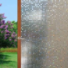 a close up of a glass door with trees in the back ground and purple flowers behind it