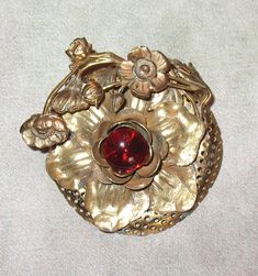 "I think that his lovely antique brooch is from the 20s but it may be from the early 30s.  It measures around 2\" in diameter and the scroll work is raised. The red glass center stone is around 1/2\" in diameter. The BONUS GIFT is a handmade fine wool black bib to wear the pin as a necklace. The bar of the brooch can sit between the layers of the necklace. There is a double fused layer of fabric at the front to support the weight of the pin plus a back lining layer with the name of the designer Vintage Red Wedding Brooches, Antique Red Brooch For Formal Occasions, Vintage Flower Brooch For Evening, Vintage Red Brooches For Formal Occasions, Antique Red Wedding Brooch, Vintage Filigree Flower Brooches, Antique Red Brooch As Gift, Antique Red Brooches As Gift, Antique Red Brooches As A Gift