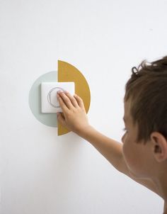 a young boy is pressing the light switch button on a white wall with an orange circle around it